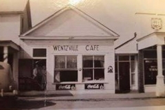 Before the Thornberry's operated Thornberry Cafeteria at the corner of Pearce and Linn, they operated the Wentzville Cafe on West Allen, next door to Wentzville Tavern. There was a pass-thru window between the cafe and the tavern - so a patron at the tavern could order food from the cafe and would prepare the order and pass the food over to the tavern. In the picture Mrs. Thornberry stands in the doorway of the Wentzville Cafe with the town pharmacist. On the back of the picture it is noted that she got new blinds for the cafe. Thanks to Trudy Thornberry Whitrock for the picture. — at West Allen in Wentzville, Missouri.